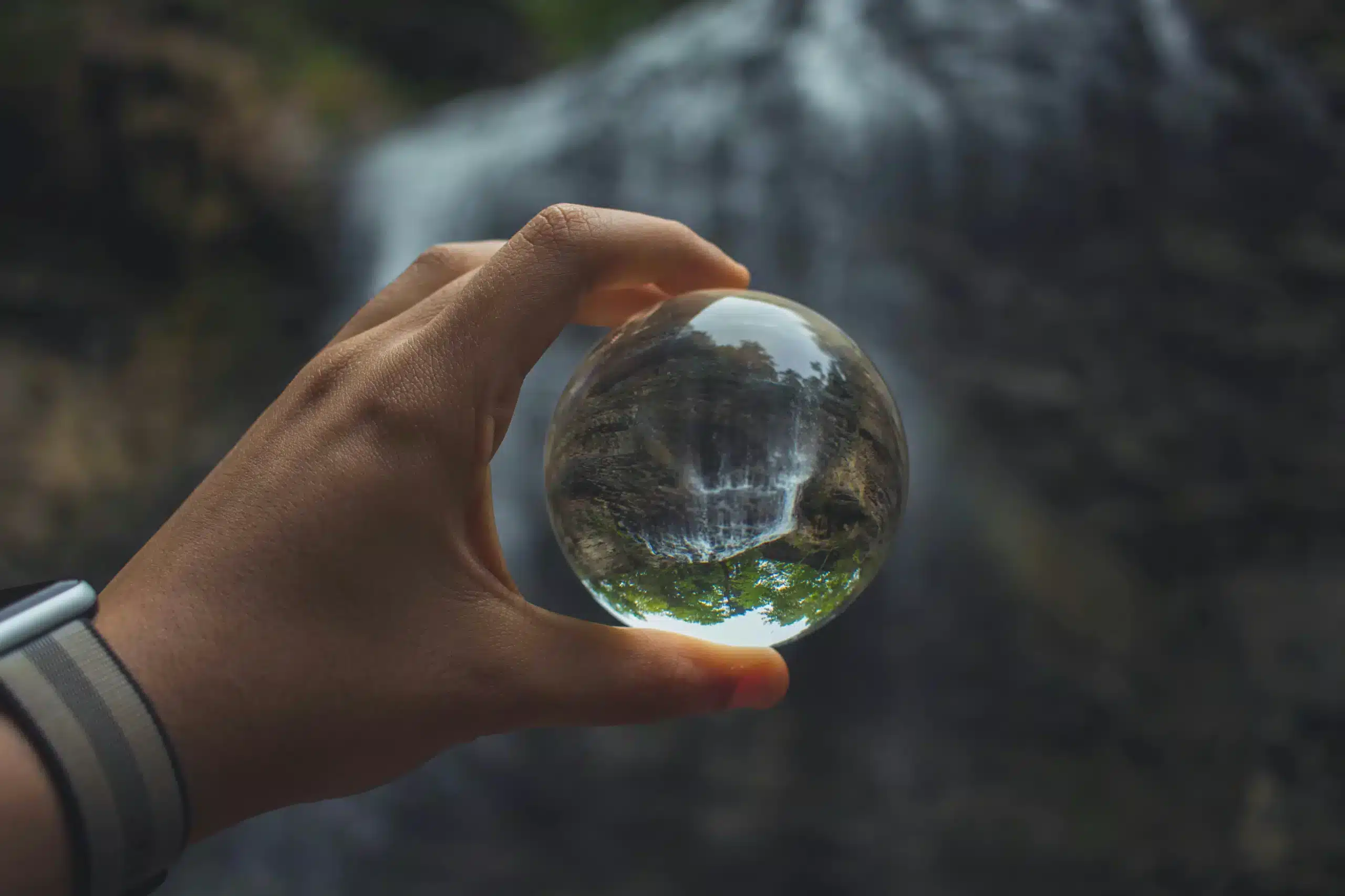 une balle en verre devant une cascade montrant la nécessité d'avoir une vision globle pour réduire son empreinte écologique